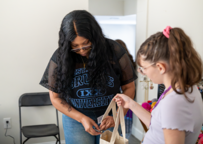 Woman and girl exchanging a canvas bag in a room, with a chair in the background.
