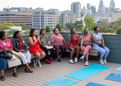 A group of women seated on a rooftop deck, with yoga mats laid out and a city skyline in the background.