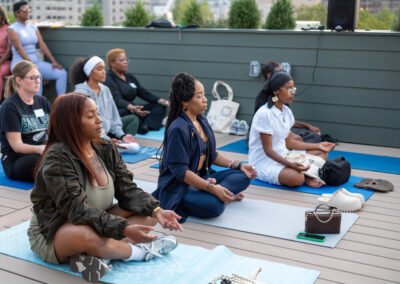 People meditating on yoga mats outdoors on a rooftop, sitting cross-legged with eyes closed, in a peaceful setting.