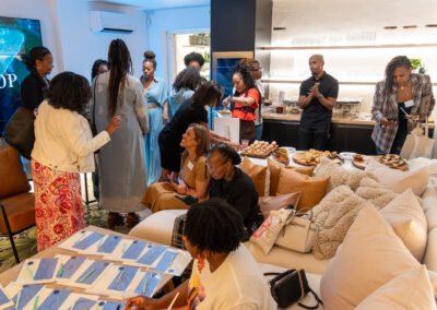 A group of people socializing at a cozy indoor gathering with snacks and seating, surrounded by notebooks and pens.