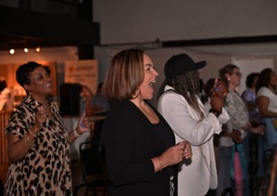 People in a dimly lit room enthusiastically clapping and cheering, some smiling and wearing casual attire.