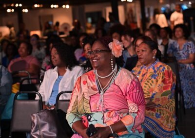 Audience seated at an event, with people wearing colorful attire and smiling under soft lighting.