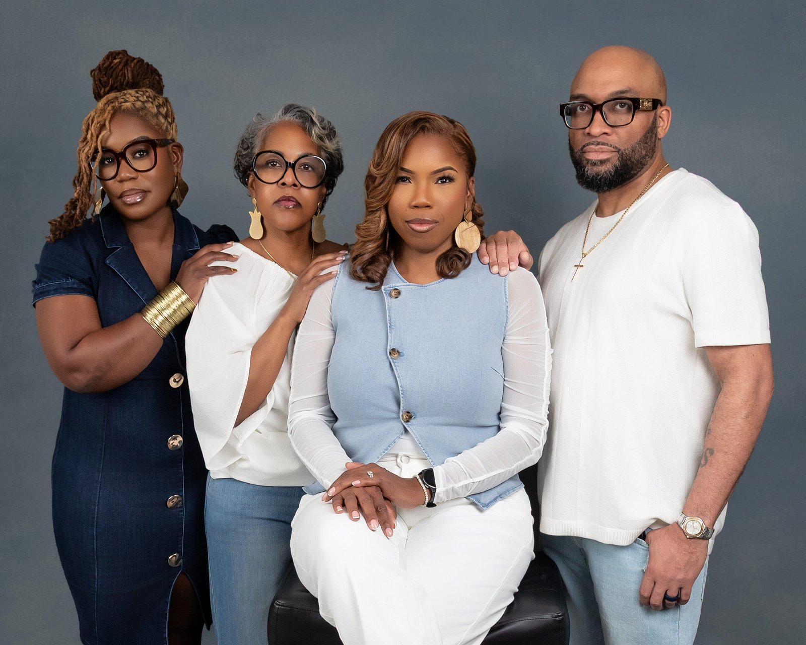 Four individuals pose together against a gray backdrop, wearing stylish and coordinated outfits.